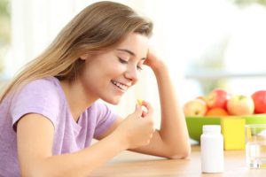 Happy teen taking a omega 3 vitamin pill on a table at home