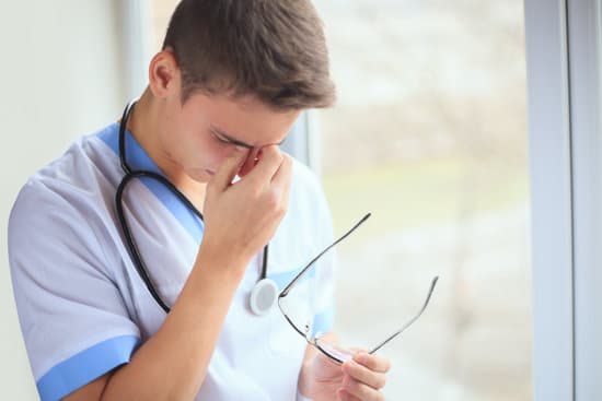 Portrait of unhappy tired young doctor having headache near a window