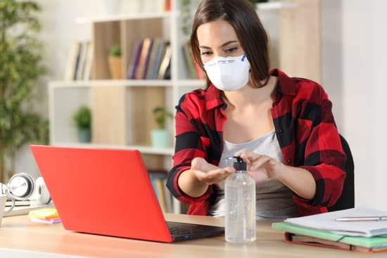 Student woman with protective mask applying hand sanitizer avoiding covid-19 sitting on a desk at home
