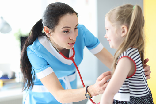 Woman doctor listening with stethoscope little girl in clinic. Diagnostics of diseases of cardiovascular system in children concept