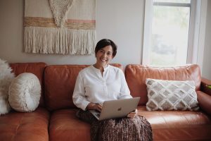 Woman sitting on a brown leather couch as she uses her laptop