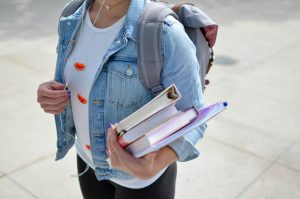 Student carrying books with one arm while wearing a backpack