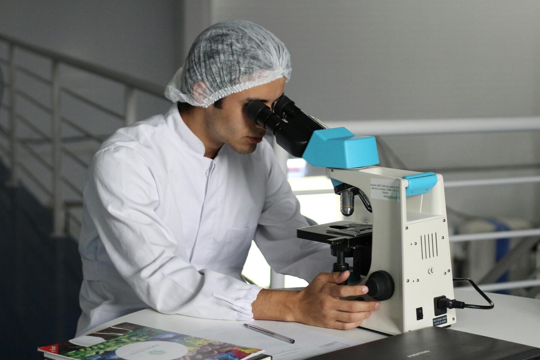 A scientist in a white lab coat examining a specimen under a microscope