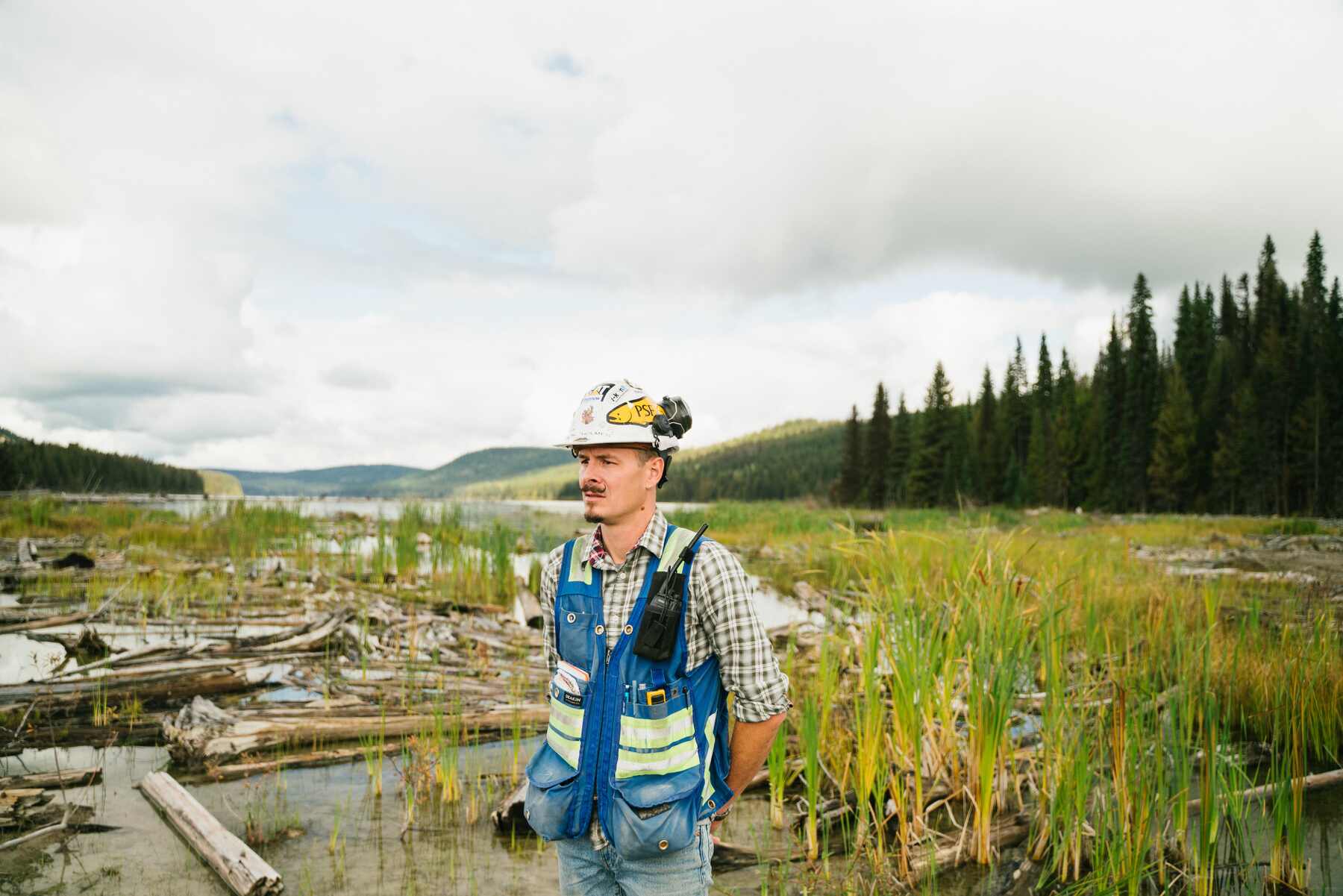 Man wearing a safety hat while observing a swamp area