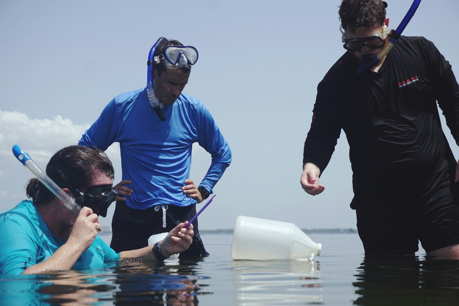 Three people wearing scuba head gear examining the sea water carefully
