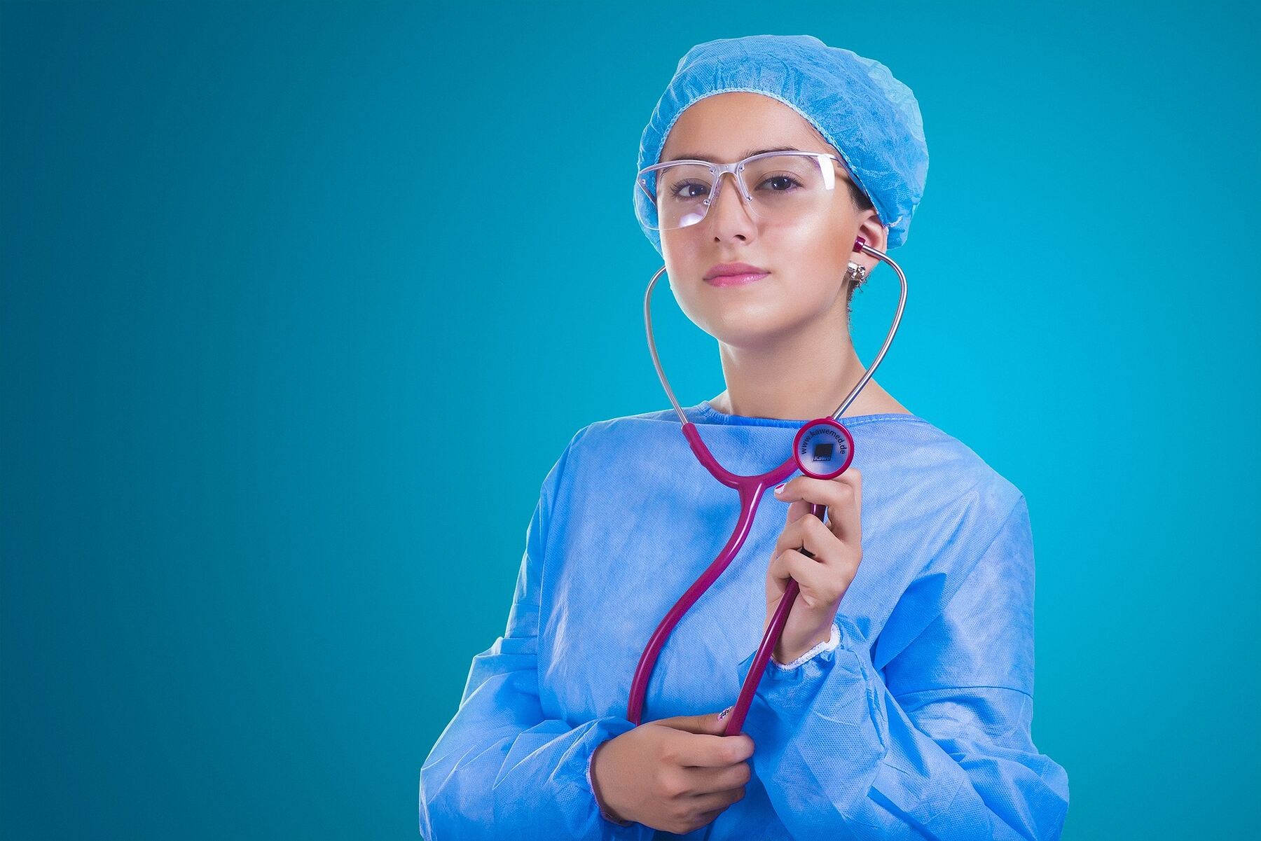 A female healthcare professional in blue scrubs holding a stethoscope