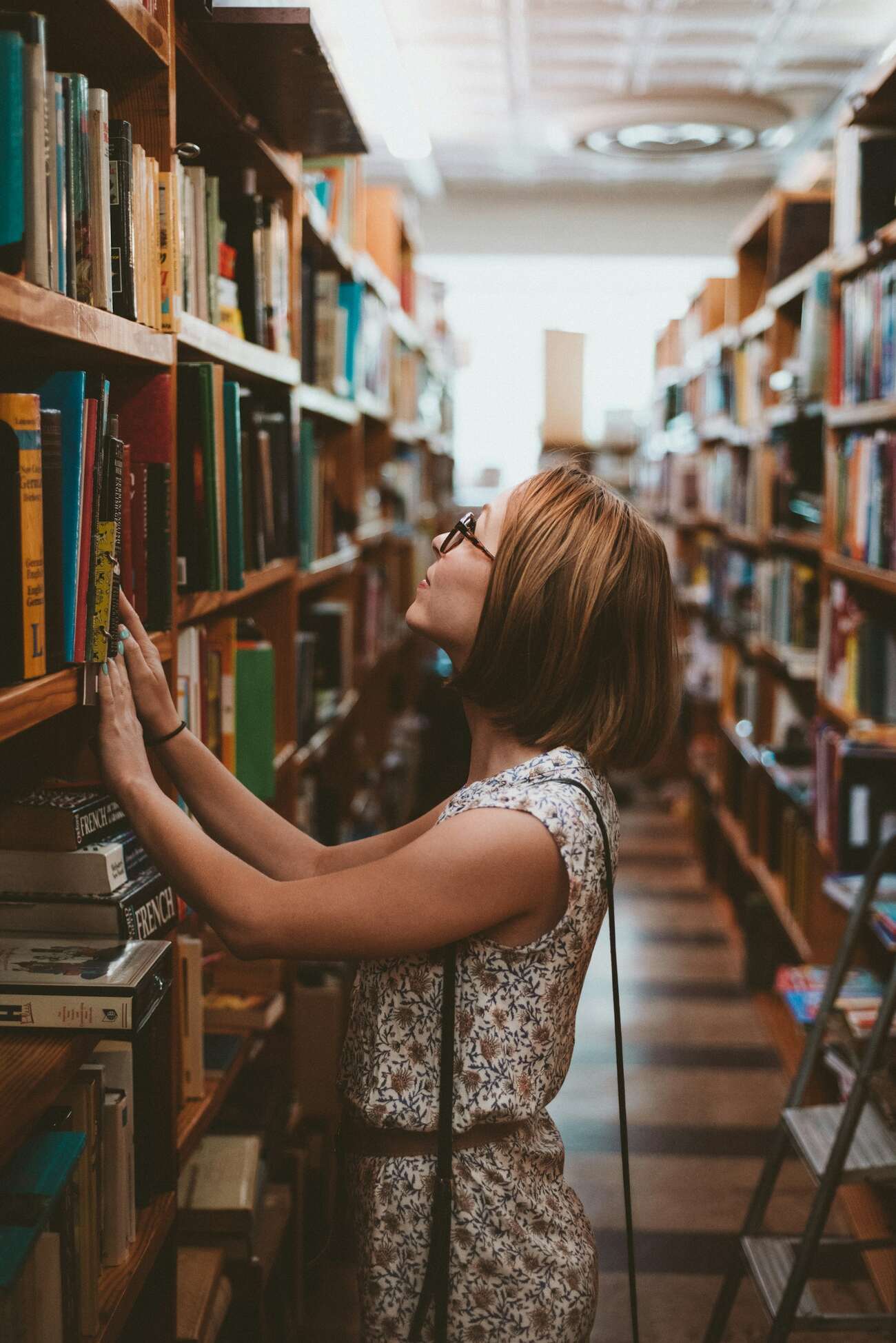 A woman browsing books in a library, surrounded by shelves filled with various titles