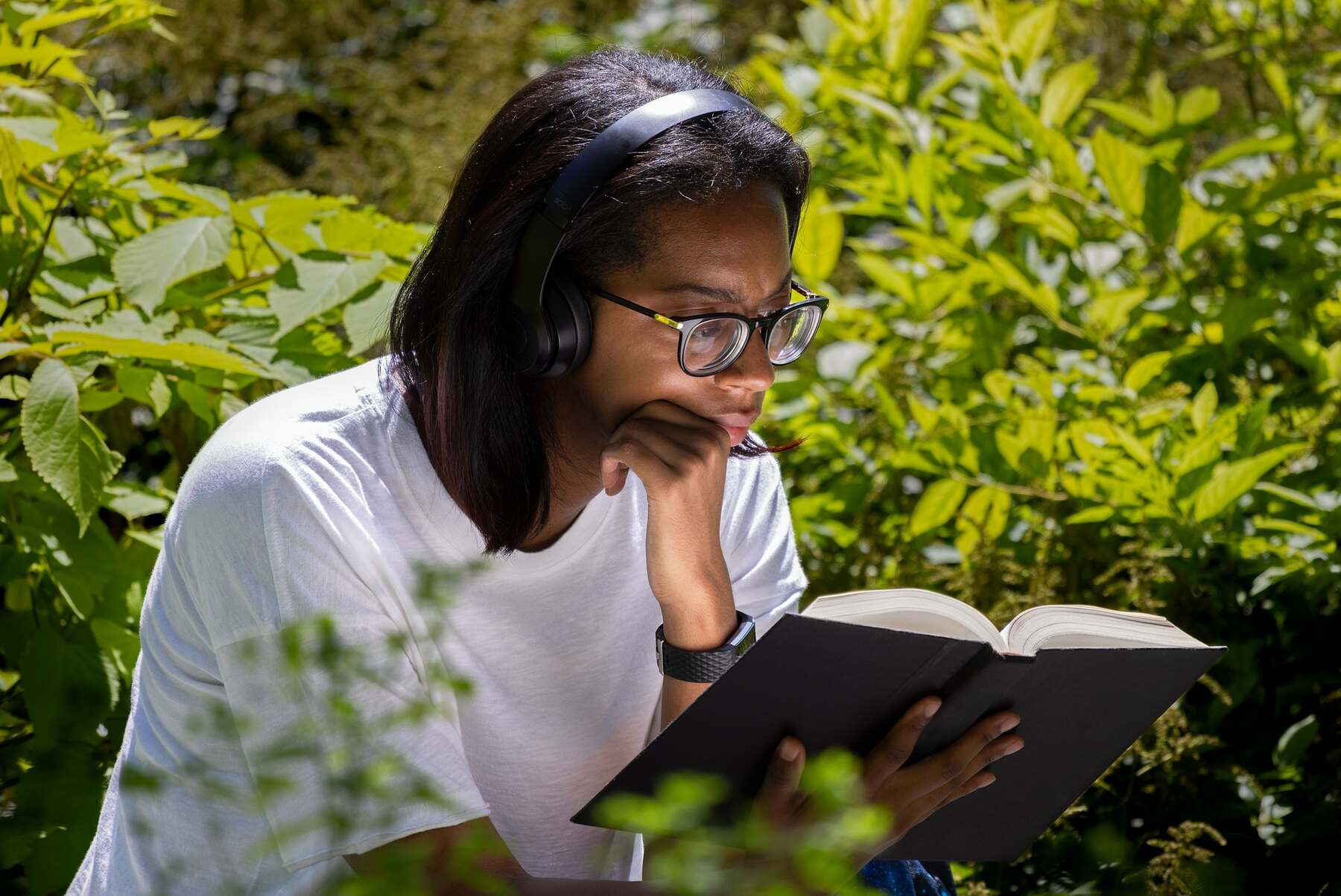 A woman with headphones reading a book on a garden
