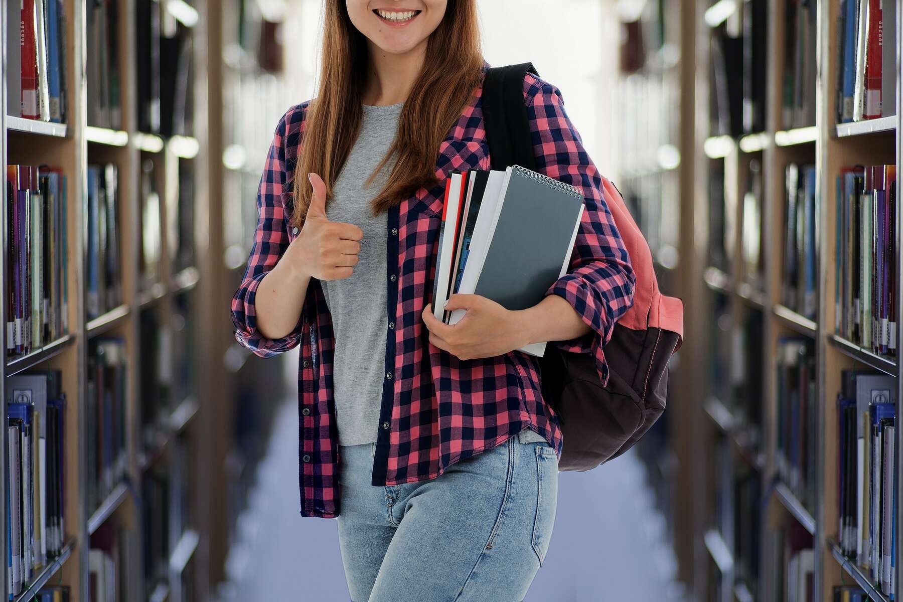 A young woman in a library, holding books and a backpack