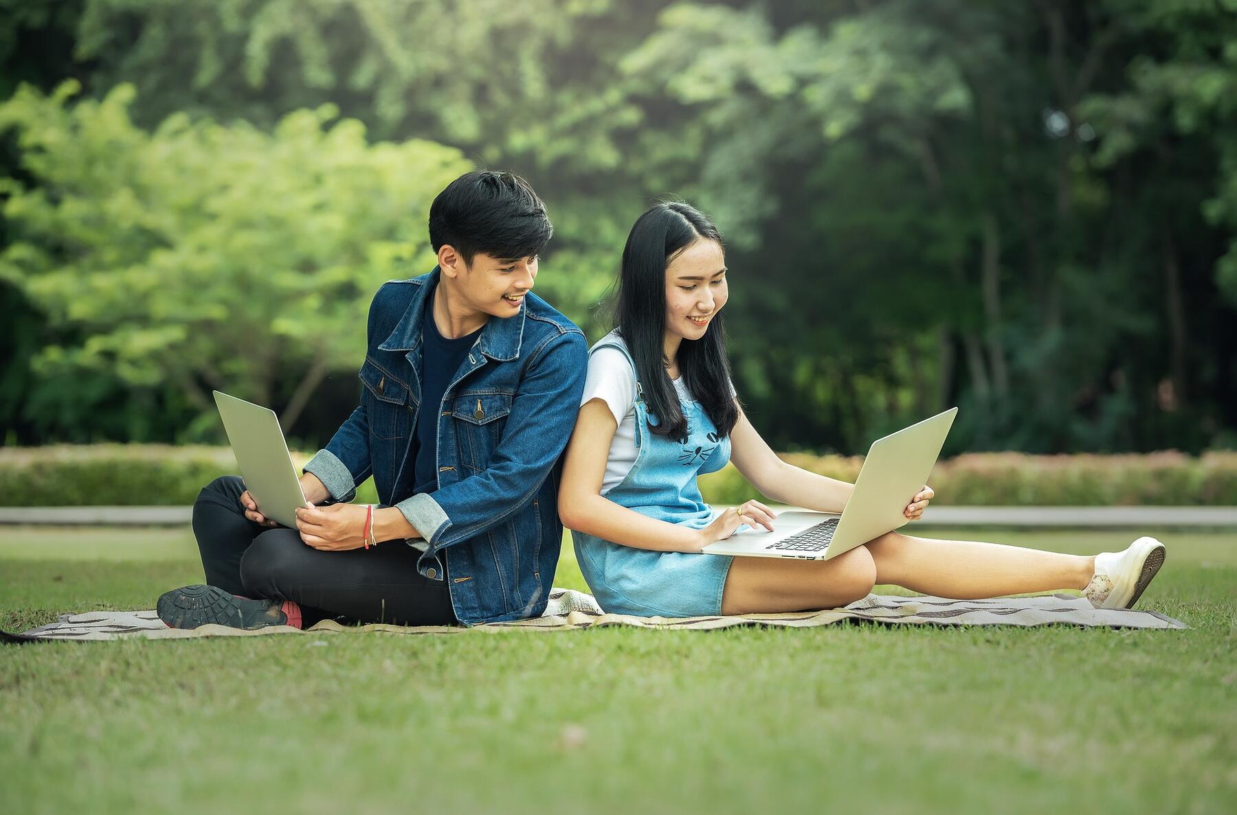 Students sitting on the grass in the park, engrossed in their laptop, enjoying the outdoors