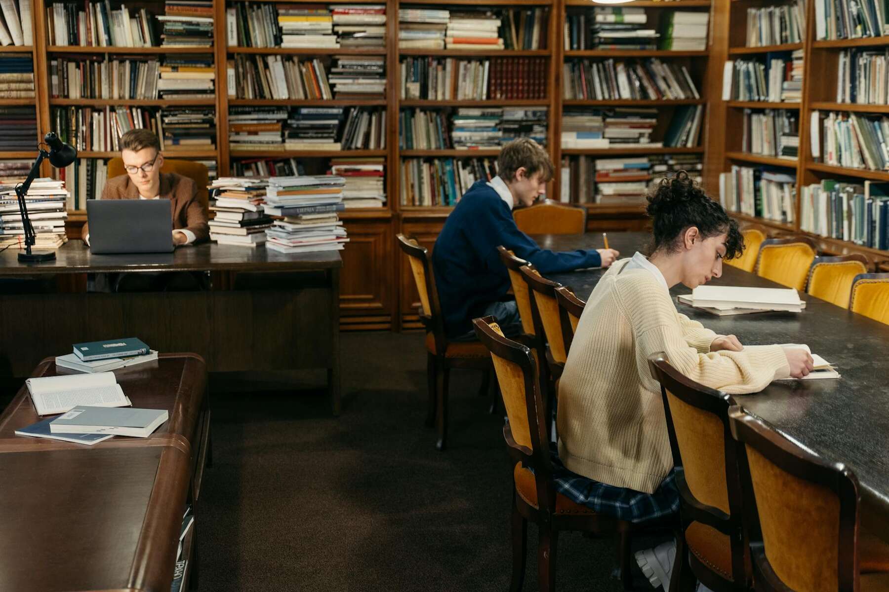 A diverse group of people sitting at tables in a library, engrossed in books and studying together