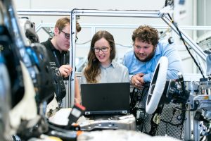Three people looking at a laptop while testing their mechanical models