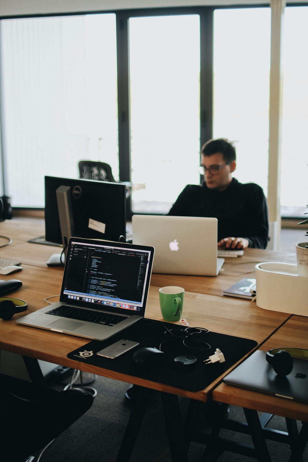 A man working on a laptop in a modern office environment with various tech devices and a coffee cup on the desk