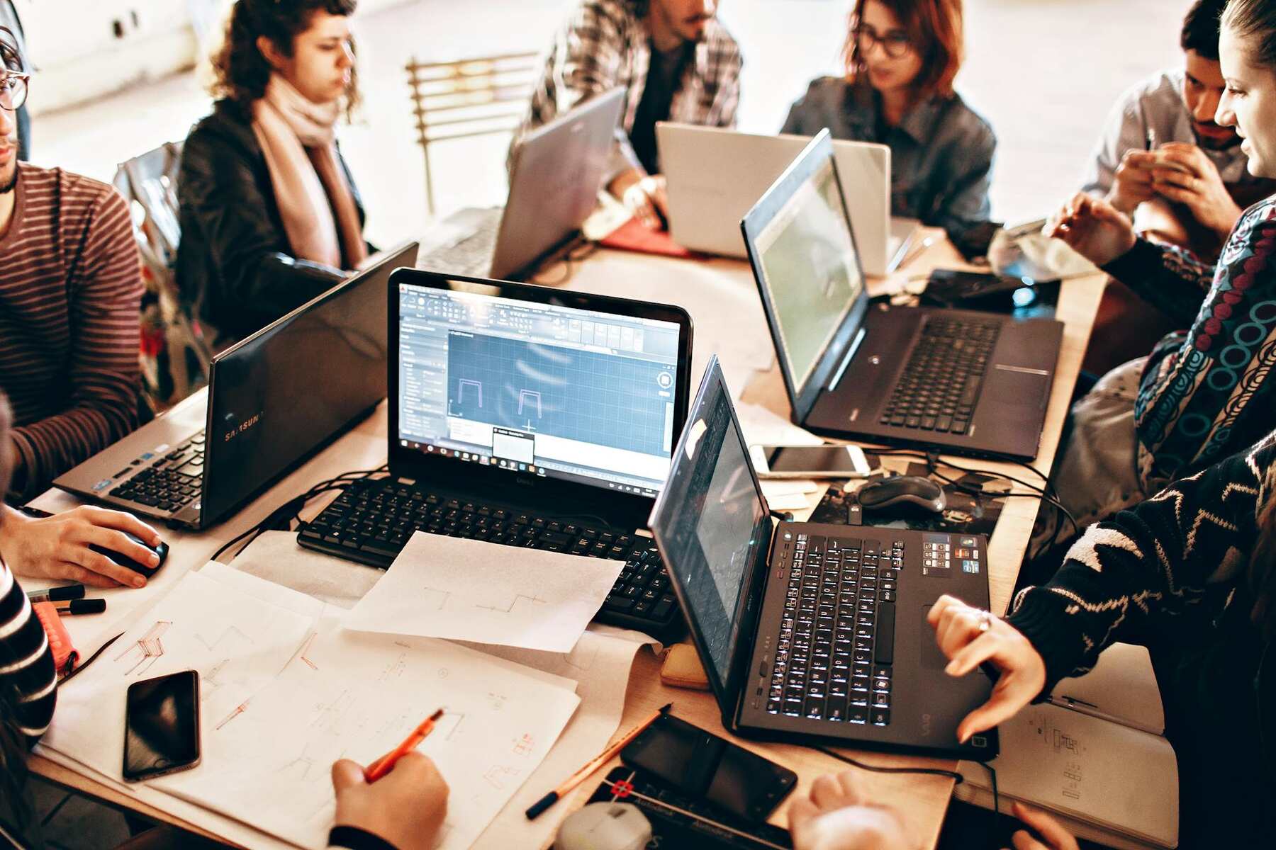 A group of young professionals collaboratively working with laptops and documents on a table in a modern office setting