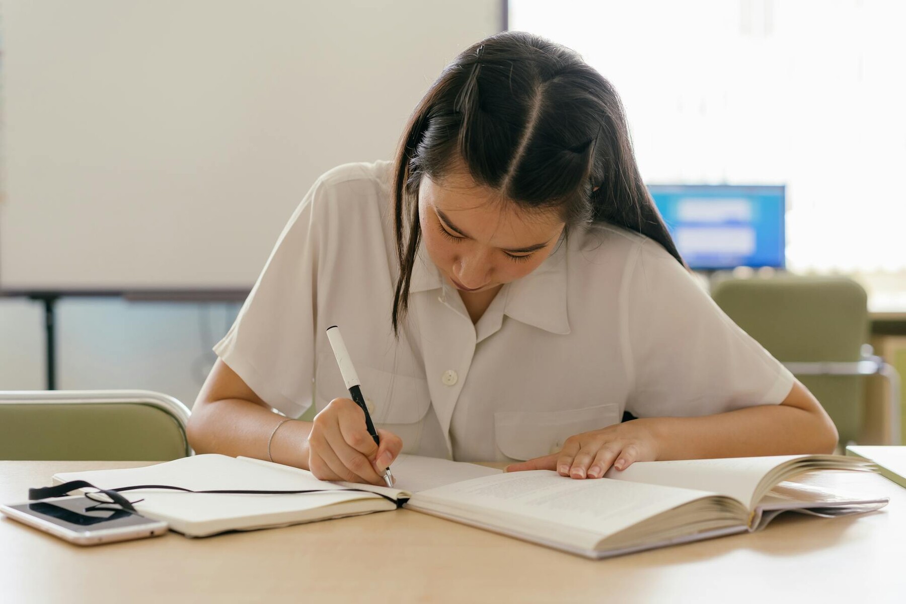 A girl focused on writing in a notebook at a desk