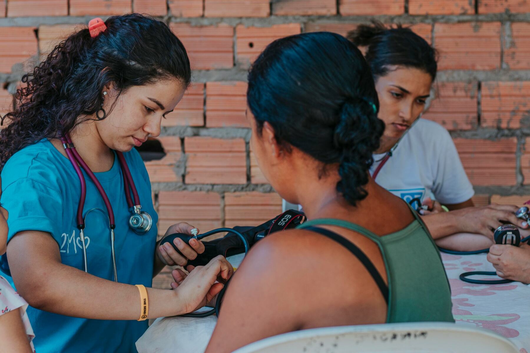 A woman in blue shirt taking another woman's blood pressure