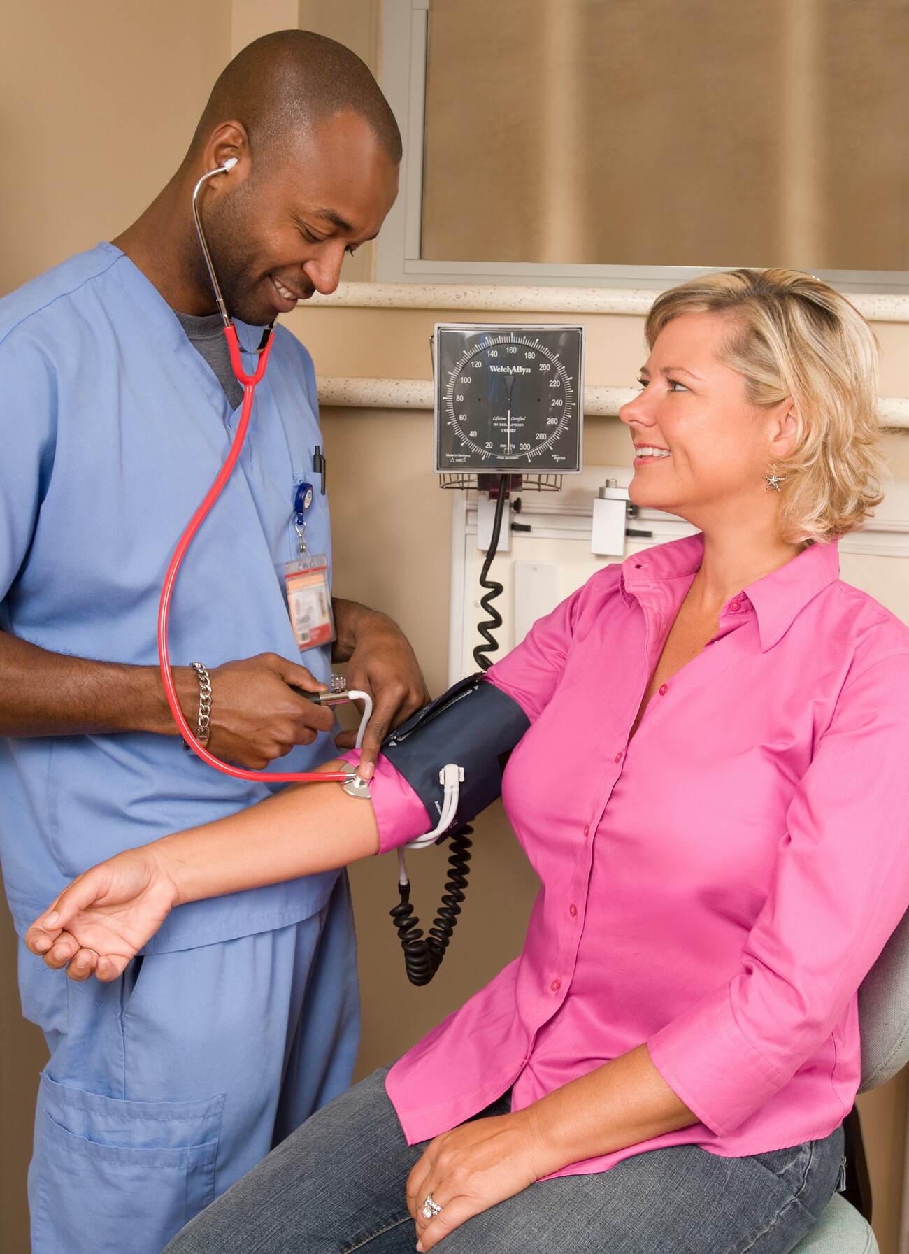 A nurse with a stethoscope and a woman sitting in a chair getting her blood pressure measured