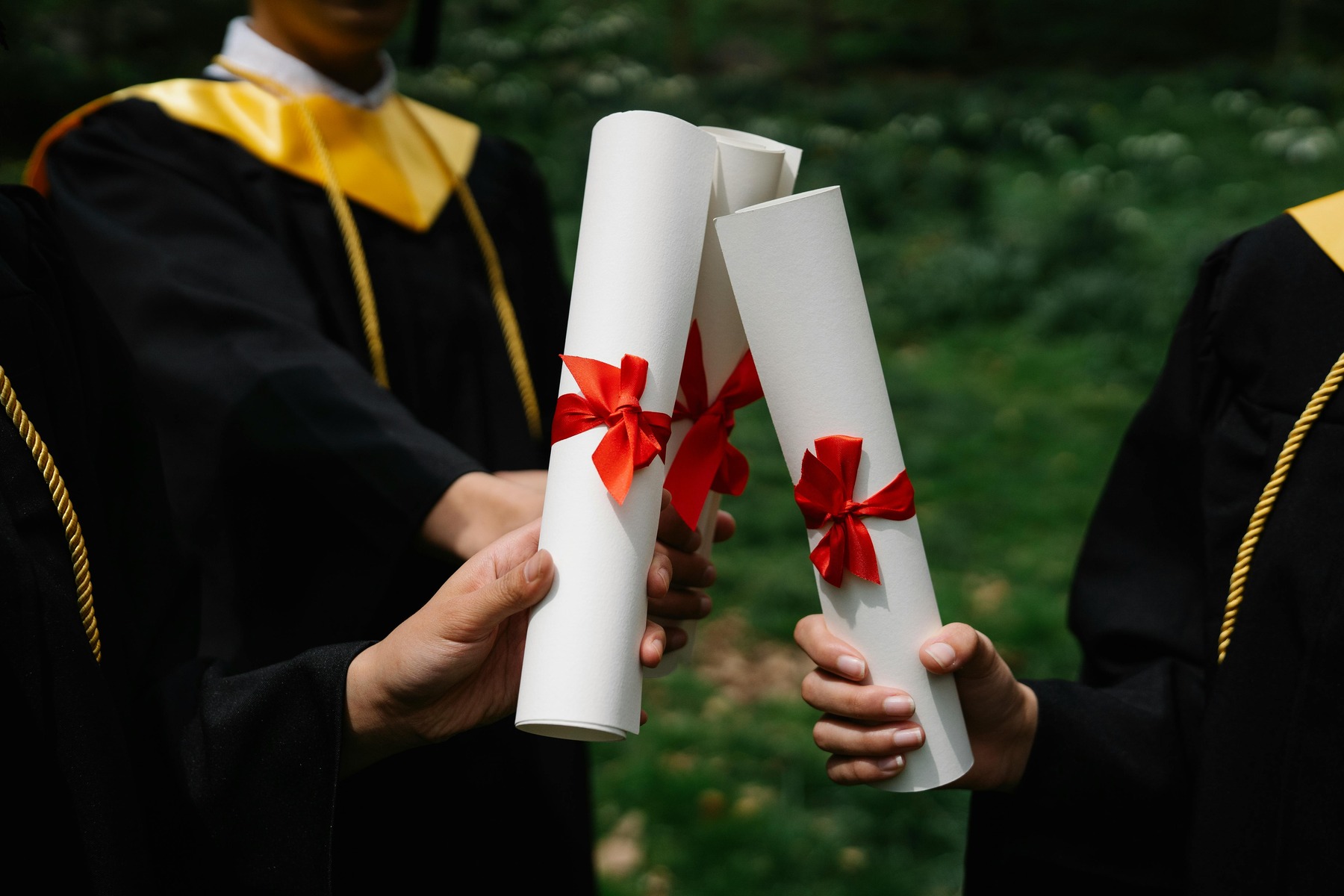 Three students wearing graduation robes, all holding diplomas