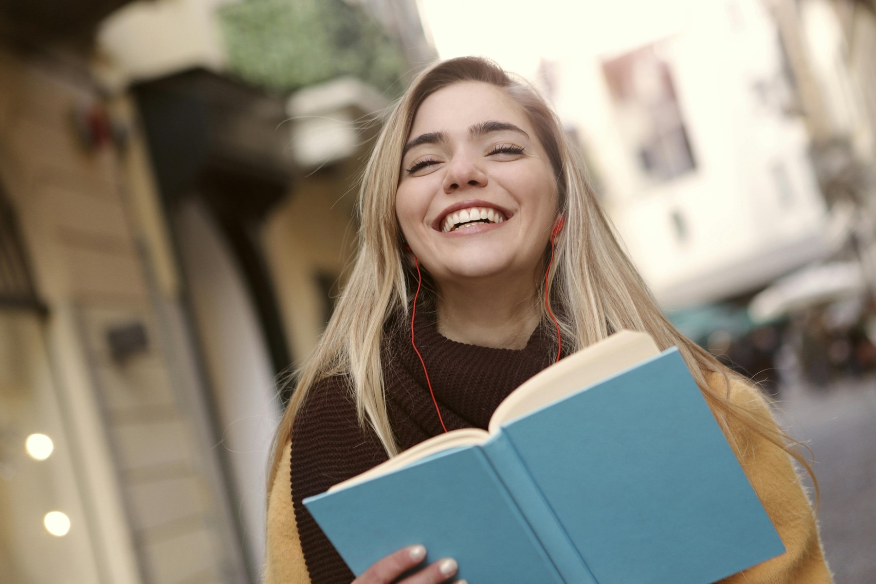 Woman smiling and wearing earphones while holding a book