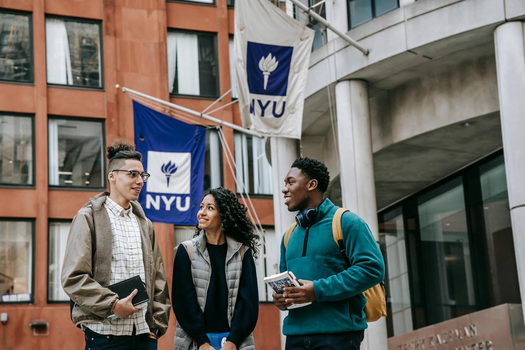 Three students engaged in conversation outside the NYU campus