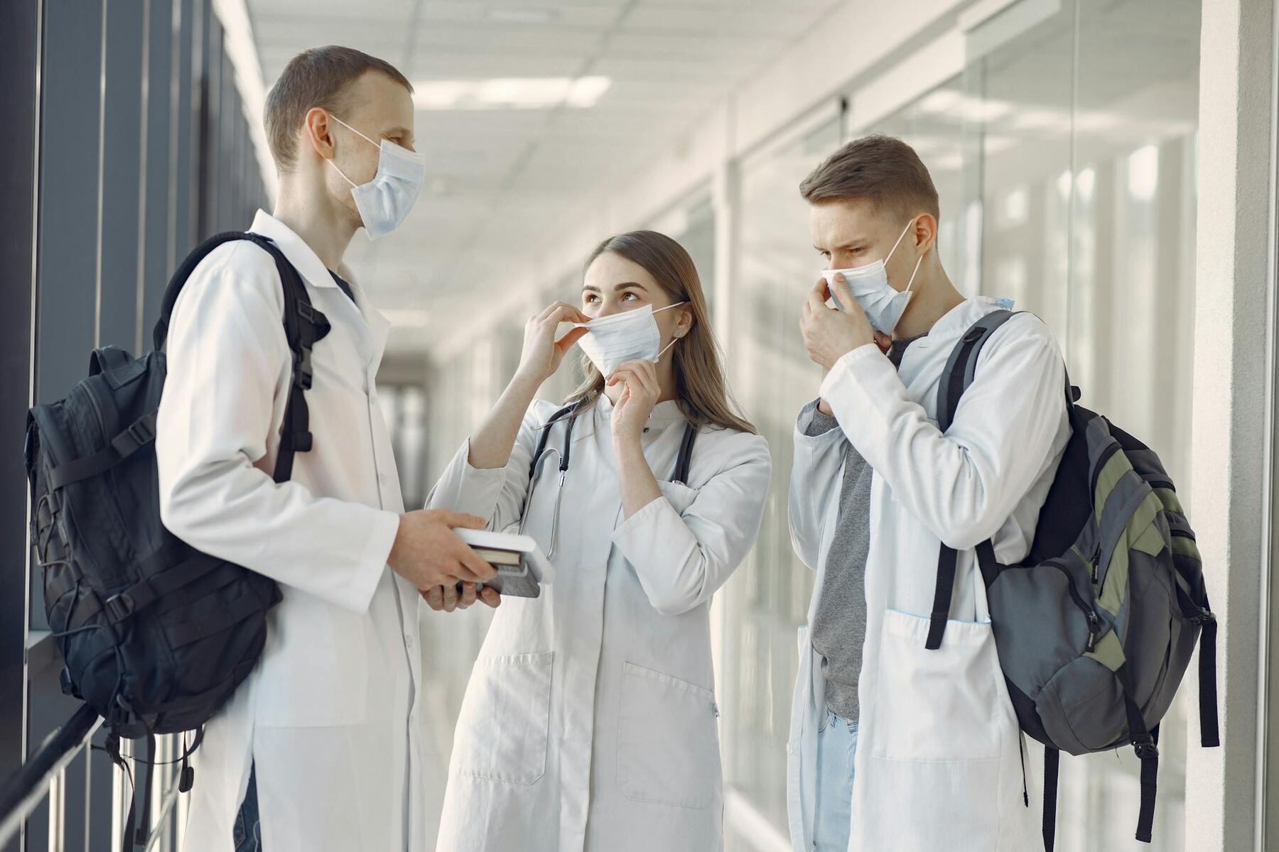 Three medical student in masks holding a book, discussing medical knowledge